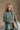 Front view of model wearing The Jennifer Sage Mock Neck Sweatshirt features sage green knit fabric, two front slit pockets, ribbed hem, high neckline and long sleeves with cuffs.