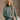 Front view of model wearing The Jennifer Sage Mock Neck Sweatshirt features sage green knit fabric, two front slit pockets, ribbed hem, high neckline and long sleeves with cuffs.