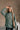 Front view of model wearing The Jennifer Sage Mock Neck Sweatshirt features sage green knit fabric, two front slit pockets, ribbed hem, high neckline and long sleeves with cuffs.