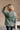 Back view of model wearing The Jennifer Sage Mock Neck Sweatshirt features sage green knit fabric, two front slit pockets, ribbed hem, high neckline and long sleeves with cuffs.