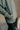 Detail view of model wearing The Jennifer Sage Mock Neck Sweatshirt features sage green knit fabric, two front slit pockets, ribbed hem, high neckline and long sleeves with cuffs.