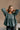 Front view of model wearing The Bella Pine Green Long Sleeve Top features pine green gauze fabric, peplum body, round neckline, long puff sleeves with elastic cuffs and open back with tie closure.