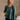 Front view of model wearing The Bella Pine Green Long Sleeve Top features pine green gauze fabric, peplum body, round neckline, long puff sleeves with elastic cuffs and open back with tie closure.