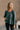 Front view of model wearing The Bella Pine Green Long Sleeve Top features pine green gauze fabric, peplum body, round neckline, long puff sleeves with elastic cuffs and open back with tie closure.