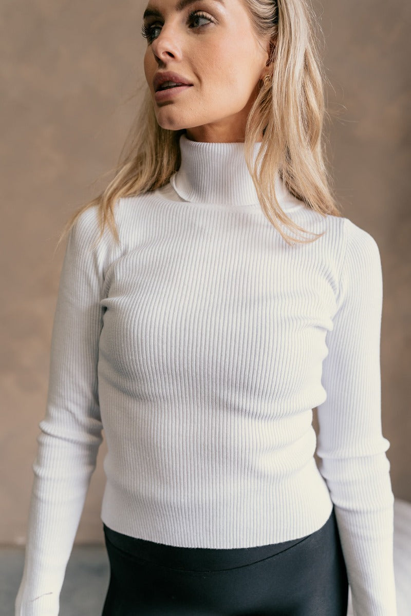 Detail view of a model wearing The Elora Off White Long Sleeve Ribbed Turtleneck features off white ribbed fabric, turtleneck neckline and long sleeves.