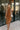 Front view of model wearing The Maria A-Symmetrical Cognac Party Dress features pale brown with a gold shimmer fabric, asymmetrical hem, pale brown lining, side cut out design with ruched design, one -shoulder strap, monochrome side zipper with hook closu