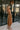 Side view of model wearing The Maria A-Symmetrical Cognac Party Dress features pale brown with a gold shimmer fabric, asymmetrical hem, pale brown lining, side cut out design with ruched design, one -shoulder strap, monochrome side zipper with hook closur