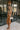 Side view of model wearing The Maria A-Symmetrical Cognac Party Dress features pale brown with a gold shimmer fabric, asymmetrical hem, pale brown lining, side cut out design with ruched design, one -shoulder strap, monochrome side zipper with hook closur
