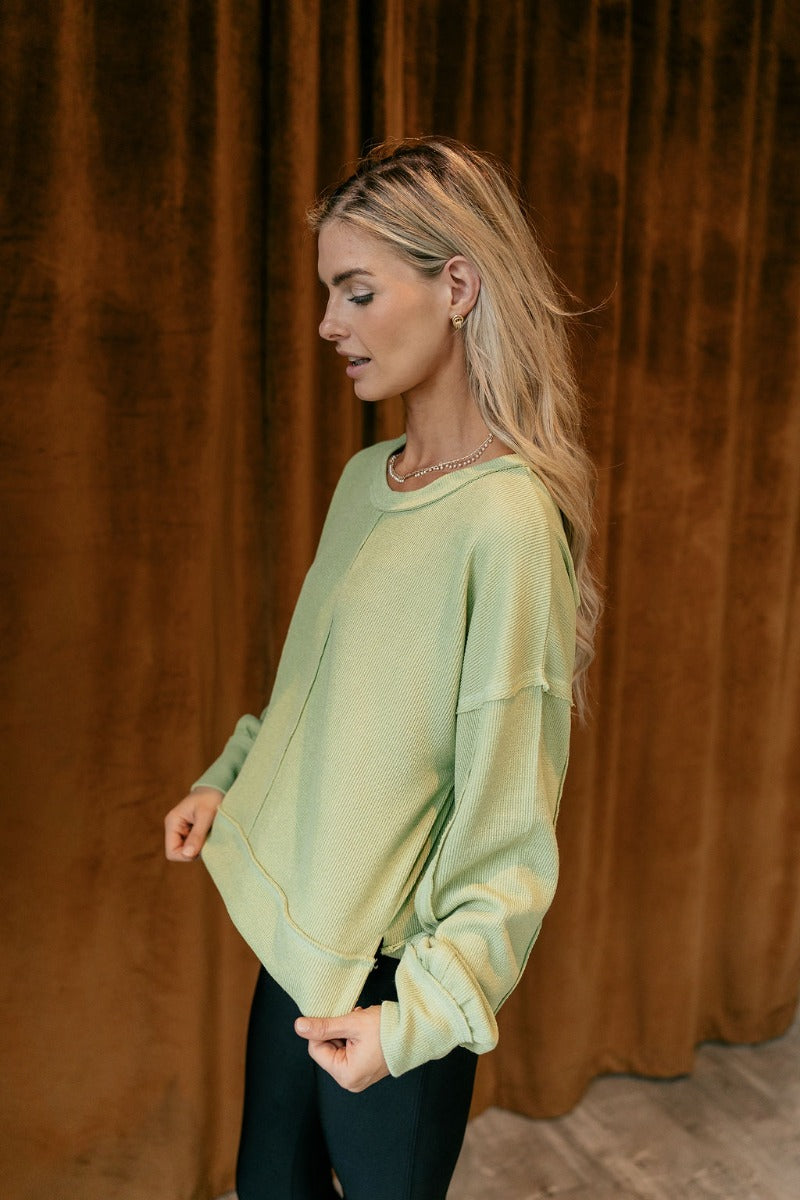 Side view of model wearing The Heather Ribbed Long Sleeve Top in Lime features lime green knit fabric, textured details, thick hem, round neckline, dropped shoulders and long balloon sleeves with cuffs.