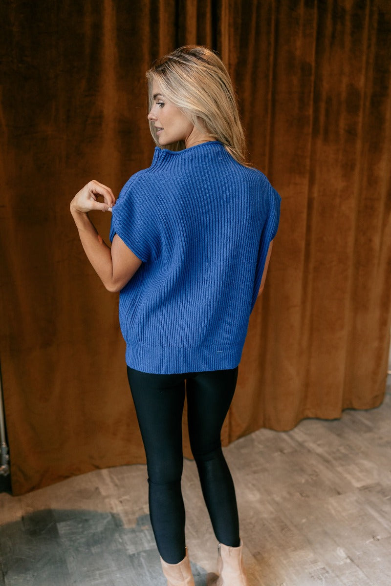 Full body back view of model wearing the Alexandra Cobalt Blue Sleeveless Sweater that has cobalt blue ribbed knit fabric, ribbed hem, high neckline and sleeveless.