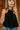 front view of model wearing the Priscilla Black Rose Detail Halter Top that has black lightweight fabric, black lining, a cropped waist, a halter strap tie neckline, and a dramatic black rosette detail.