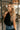 Side view of model wearing the Priscilla Black Rose Detail Halter Top that has black lightweight fabric, black lining, a cropped waist, a halter strap tie neckline, and a dramatic black rosette detail.