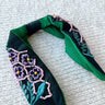 Flat lay of the Flower Power Headband which features emerald coloring fabric, turquoise and purple stitching, floral pattern with pink and yellow beads.