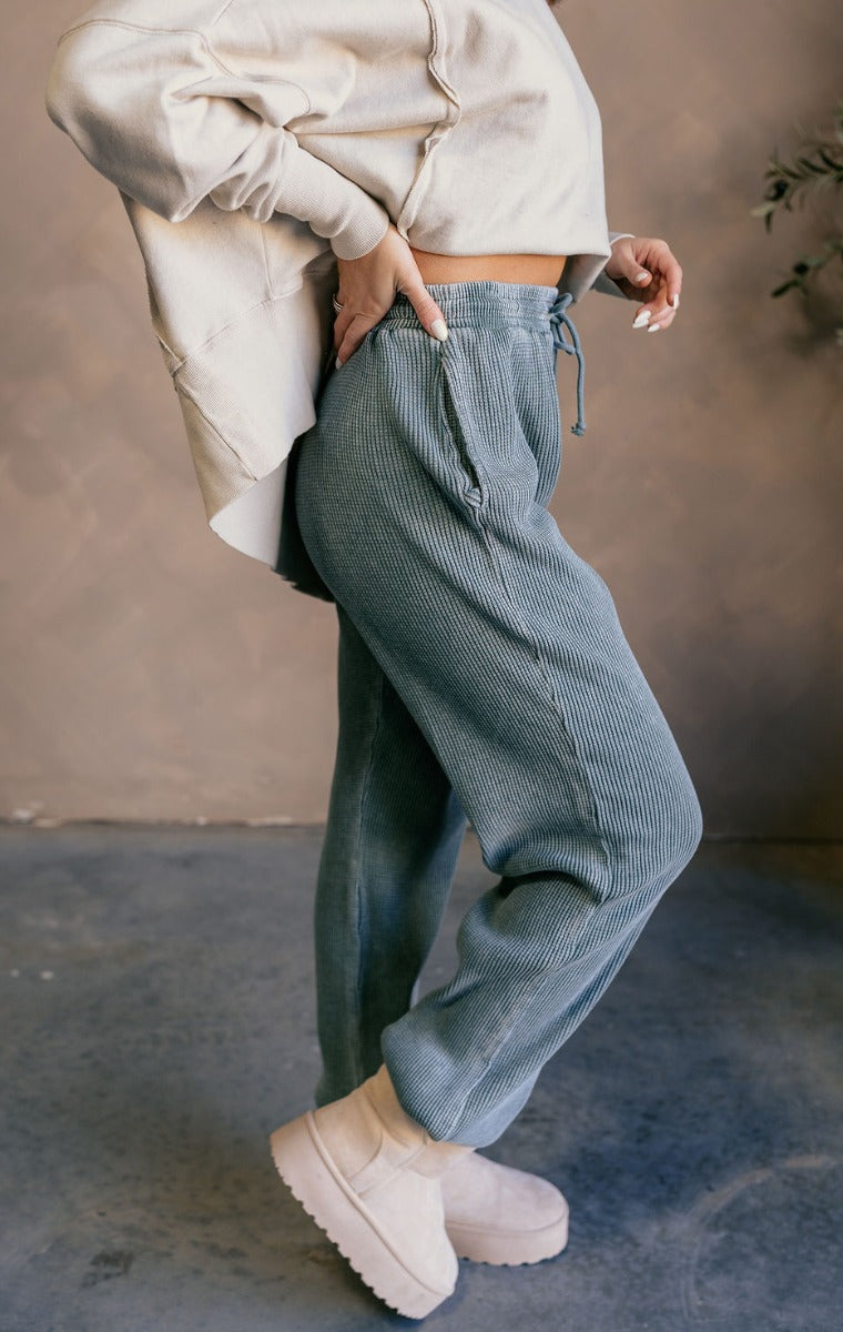Side view of model wearing the Myla Grey Green Drawstring Jogger Pants which features grey green waffle knit fabric, two front pockets, an elastic waistband with drawstring ties, and jogger pant legs with thick hem.