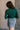 Back view of model wearing the Elora Green Long Sleeve Ribbed Turtleneck that has pine green ribbed fabric, a turtleneck neckline, and long sleeves.