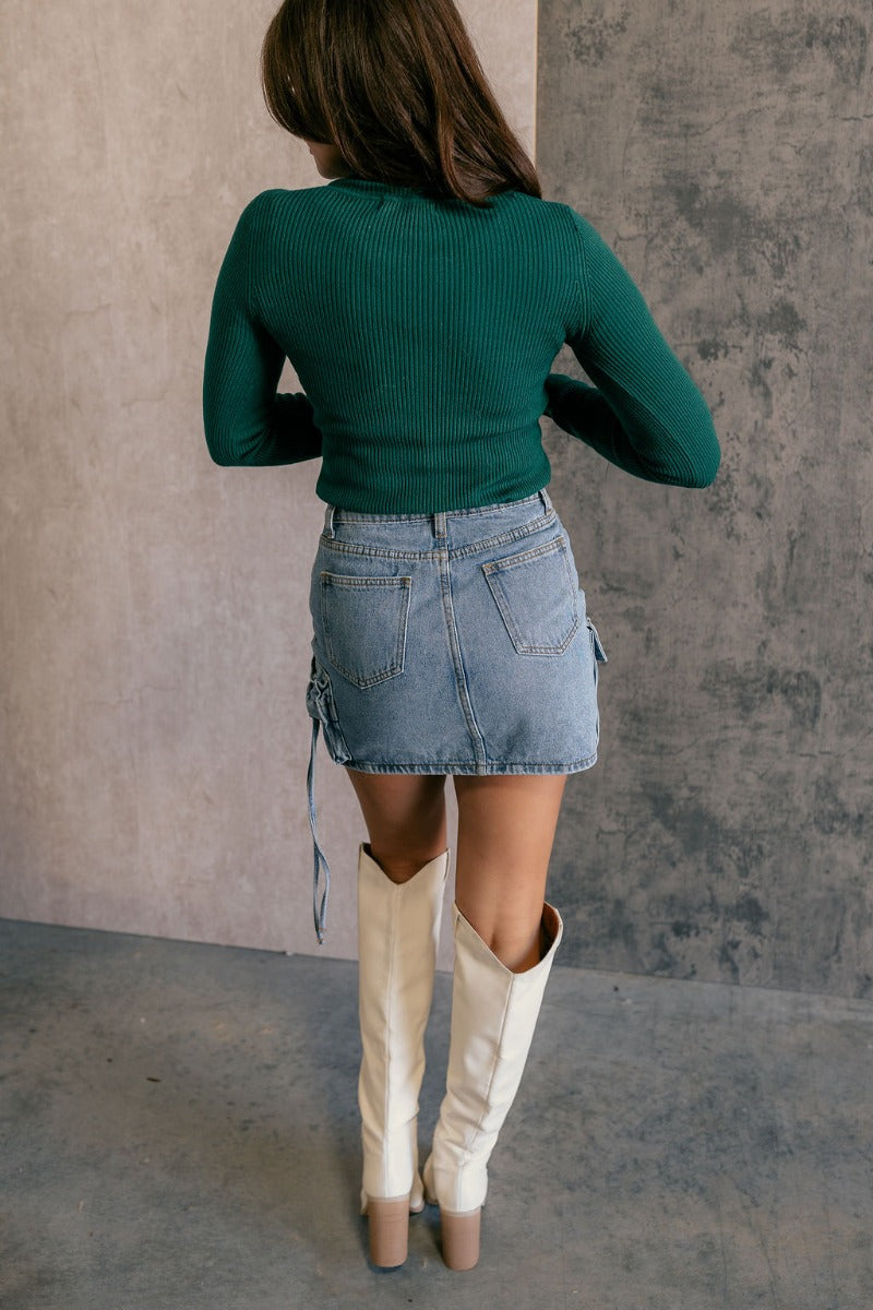 Full body back view of model wearing the Elora Green Long Sleeve Ribbed Turtleneck that has pine green ribbed fabric, a turtleneck neckline, and long sleeves.