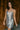 front view of model wearing the Elia Silver Sequin Sleeveless Mini Dress that has light grey knit fabric covered in silver mirror sequins, silver lining, mini length, a v-neckline, and halter spaghetti straps.