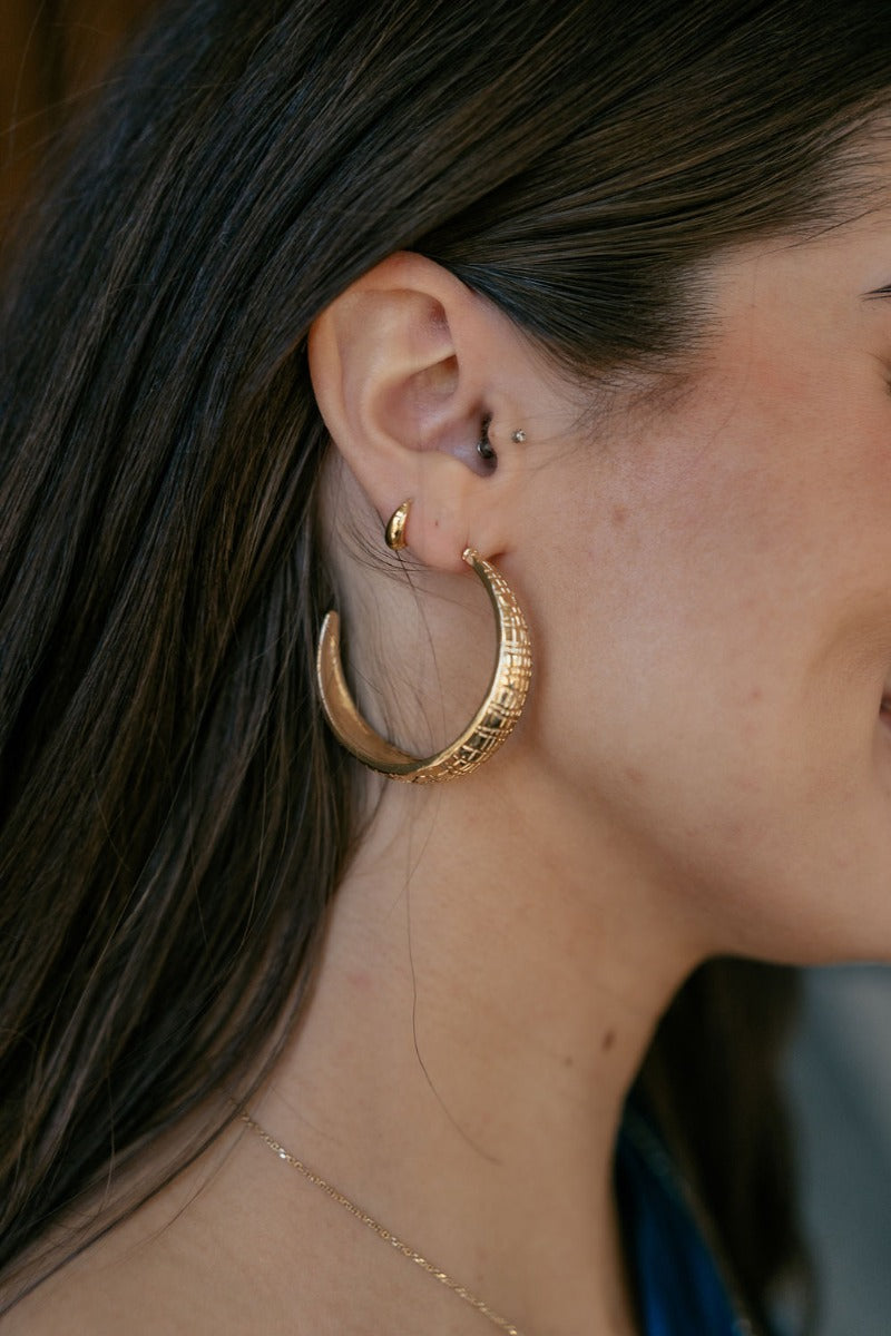 Side view of model wearing the Lila Gold Textured Hoop which features large open, gold hoops with textured details.