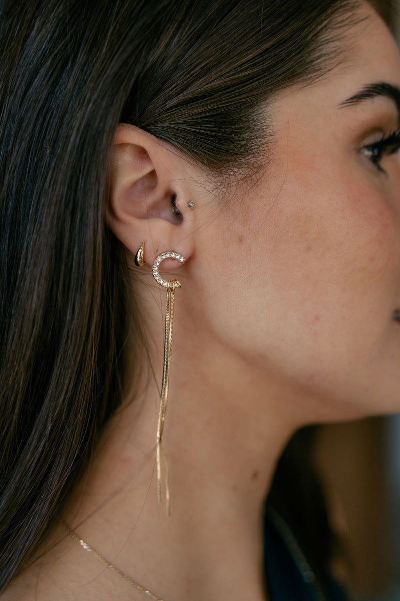 Side view of model wearing the Orla Gold and Rhinestone Stud Fringe Earring which features u-shaped studs with clear stones attached to two gold strands.