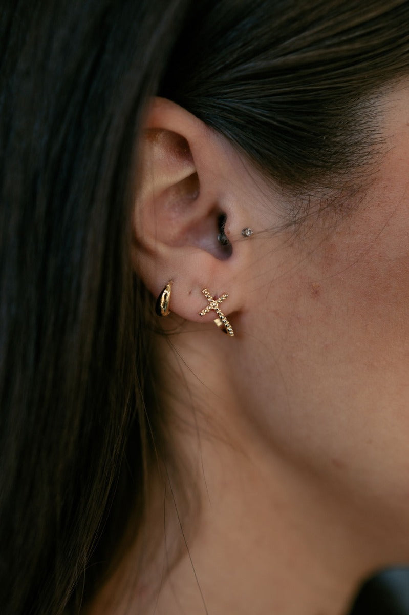 Side view of model wearing the Grace Gold Cross Stud Earring which features mini gold, open cross shaped huggies with hobnail design.