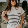 Front view of model wearing the Katelyn White & Navy Striped Sleeveless Sweater that has white and navy knit fabric, a striped pattern, a mock neckline, and a sleeveless design.