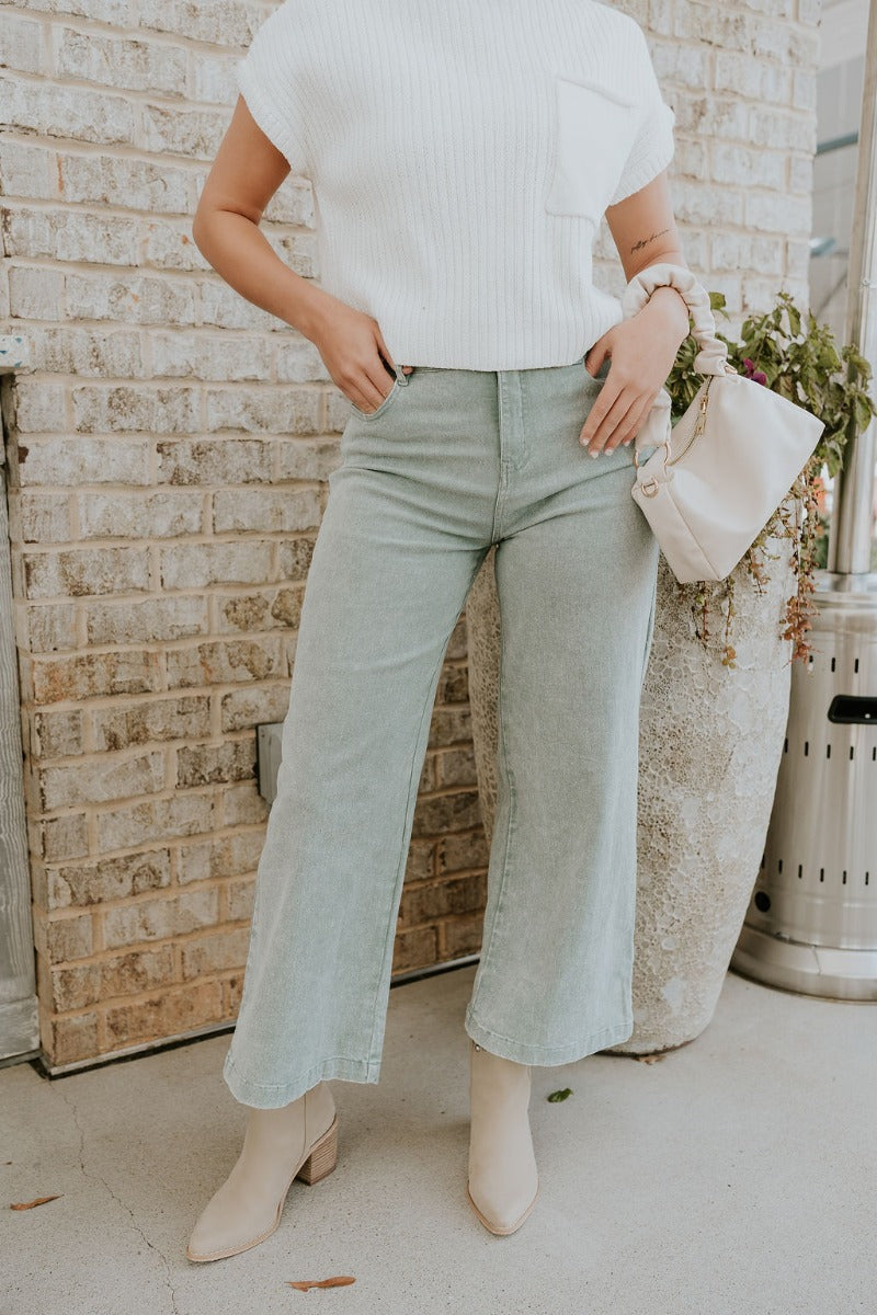 Front view of model wearing the Livia Sage Wide Leg Pants that has sage green washed denim-like fabric, a front zipper with a button closure, belt loops, front pockets, back pockets and wide pant legs.