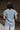 Back view of model wearing the Cynthia Blue Short Sleeve Button Up Top that has light blue tencel fabric, light brown stitching , grey tortoise buttons, a collared neckline, and short flare sleeves.