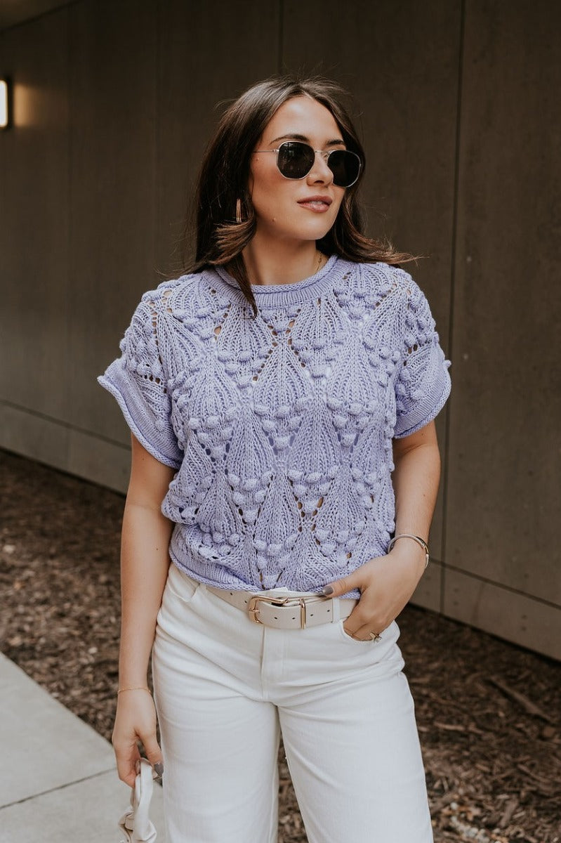 Front view of model wearing the Megan Periwinkle Crochet Short Sleeve Sweater that has lavender-blue crochet knit fabric, monochrome 3d polka dot details, ribbed hem, a round neck, and short sleeves.