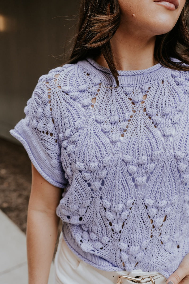 Close front view of model wearing the Megan Periwinkle Crochet Short Sleeve Sweater that has lavender-blue crochet knit fabric, monochrome 3d polka dot details, ribbed hem, a round neck, and short sleeves.