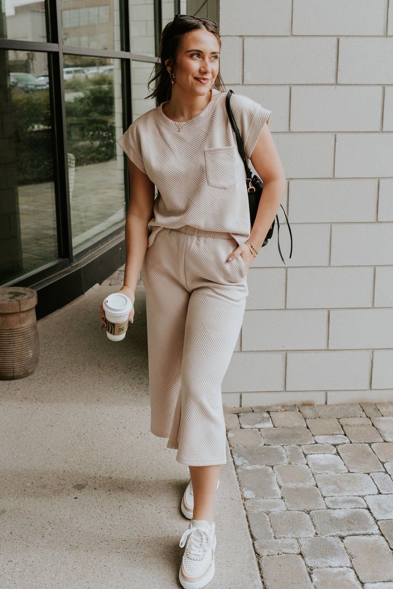 Full body view of model wearing the Ella Light Taupe Cropped Pants which features light taupe knit fabric, monochrome block stripe design, elastic waistband, two front slit pockers and cropped wide pant legs.