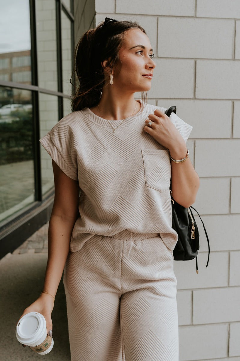 Front view of model wearing the Ella Light Taupe Short Sleeve Top which features light taupe knit fabric, monochrome block stripe design, front left chest pocket, round neckline and short sleeves.