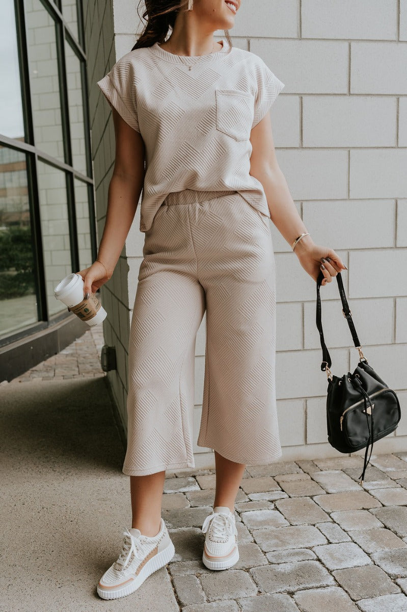 Front view of model wearing the Ella Light Taupe Cropped Pants which features light taupe knit fabric, monochrome block stripe design, elastic waistband, two front slit pockers and cropped wide pant legs.