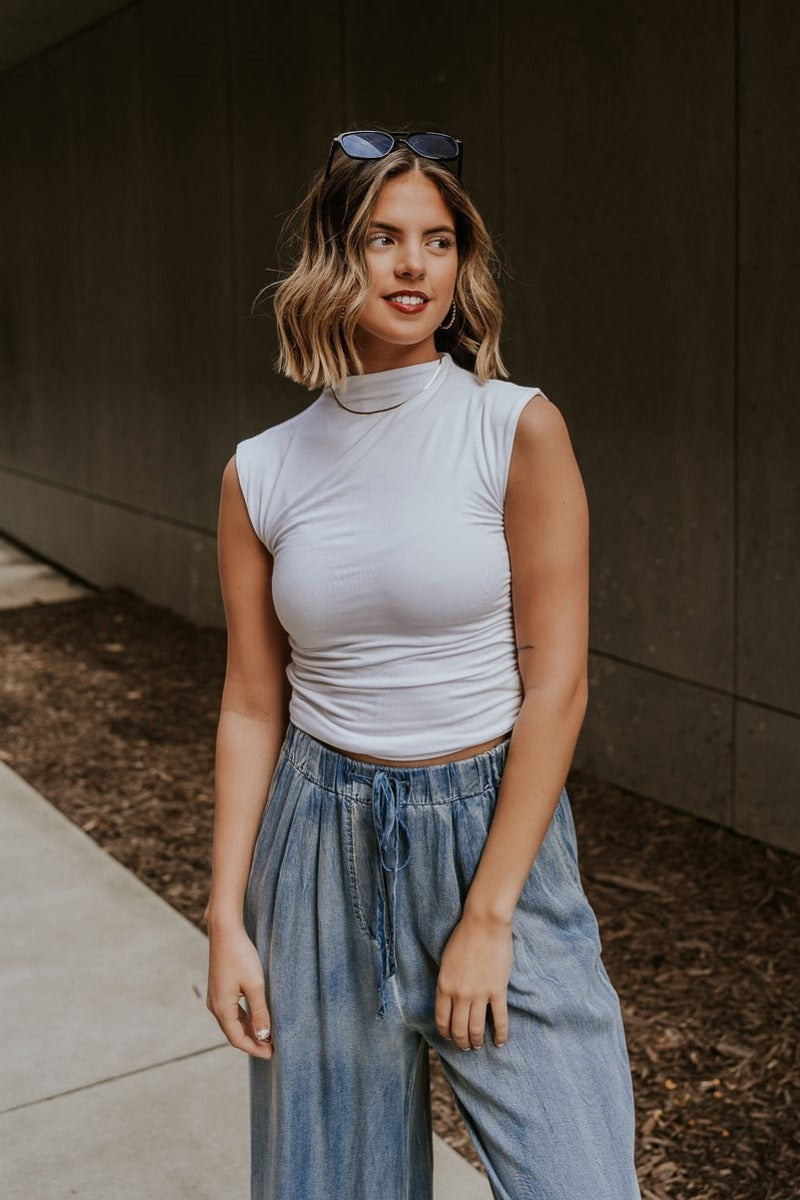 front view of model wearing the Rebekah White Ruched Mock Neck Tank Top that has double layer white knit fabric, ruched side details, a high neckline, and a sleeveless design.