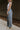 Side view of model wearing the Kelly Blue Wide Leg Drawstring Pants that have blue denim-washed light weight fabric, two front slit pockets, an elastic waistband with a drawstring tie, and wide pant legs.