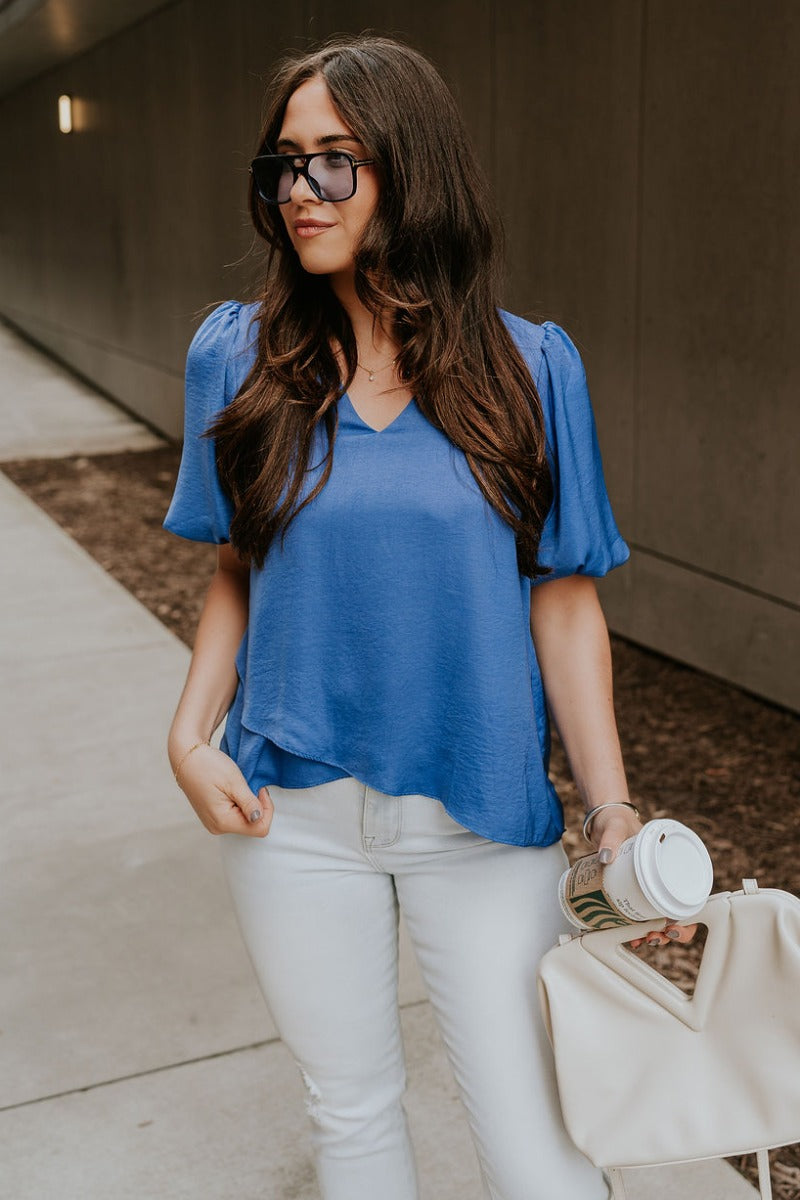 Front view of model wearing the Addison Blue Short Puff Sleeve Top which features cobalt blue satin fabric, front black lining, a v-neckline, and short puff sleeves.