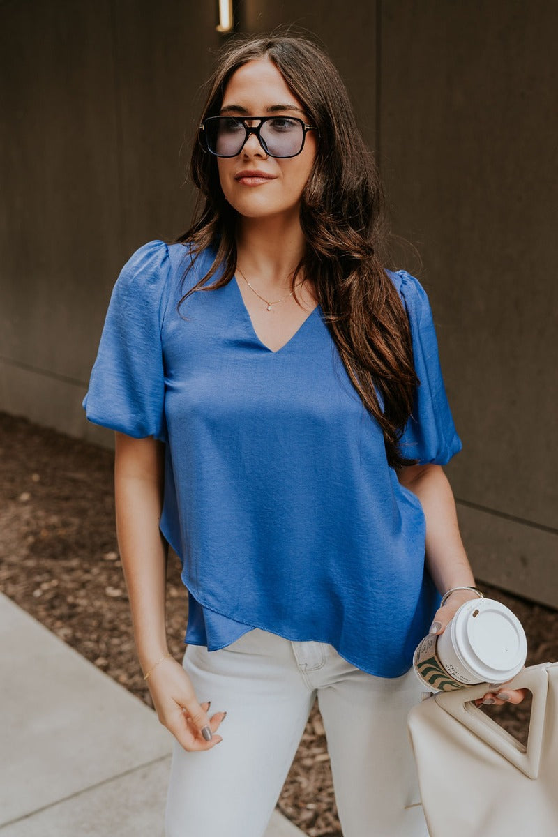 Front view of model wearing the Addison Blue Short Puff Sleeve Top which features cobalt blue satin fabric, front black lining, a v-neckline, and short puff sleeves.