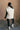 Full body back view of model wearing the Reagan White Oversized Puffer Vest that has white lightweight puffer fabric, a 3 tiered design, white lining, two pockets, a hidden zipper, snaps, a high neck and a sleeveless design.