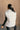 Back view of model wearing the Reagan White Oversized Puffer Vest that has white lightweight puffer fabric, a 3 tiered design, white lining, two pockets, a hidden zipper, snaps, a high neck and a sleeveless design.