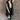 Full body front view of model wearing the Camryn Black Longline Puffer Vest features black puffer fabric, midi length, pockets, a hidden zipper with snap closures, a high neck, and a hood with drawstring ties.