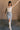 Full body front view of model wearing the Liana Denim Front Slit Midi Skirt that has light wash denim fabric, brown stitching, midi length, a raw hem, and a front slit.