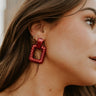 Side view of model wearing the Alina Red Earrings that have red metallic roped open rectangles with studs attached.
