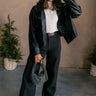 Full body front view of model wearing the Margo Black Denim Cargo Pants that have black cotton fabric, pockets, a front zipper with a button closure, belt loops, and wide legs.