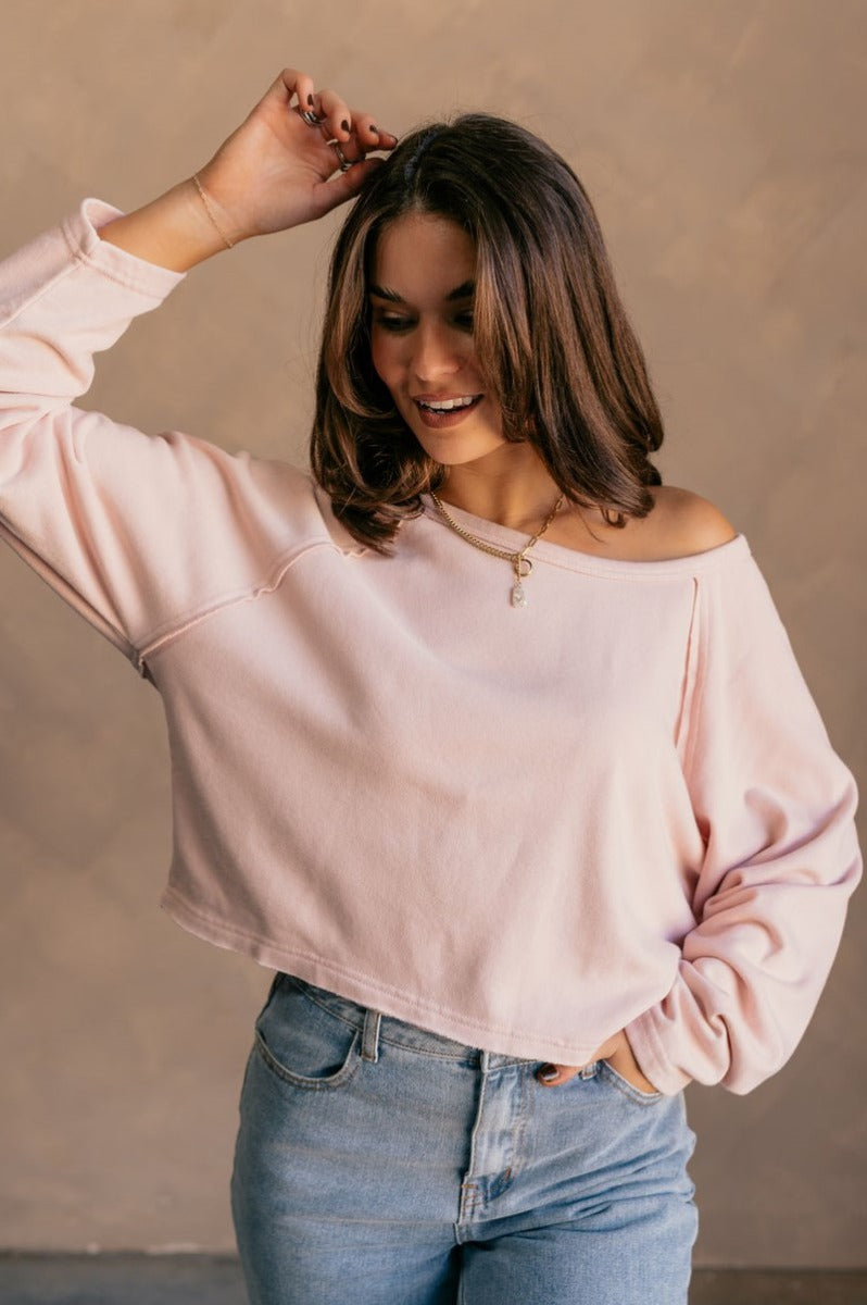 front view of model wearing the Charlotte Light Pink Raglan Sweatshirt that has light dusty pink knit fabric, raw hem details, a round neckline, and long wide sleeves.