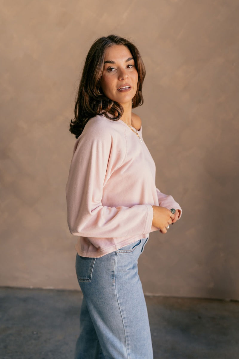 Side view of model wearing the Charlotte Light Pink Raglan Sweatshirt that has light dusty pink knit fabric, raw hem details, a round neckline, and long wide sleeves.