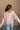 Back view of model wearing the Charlotte Light Pink Raglan Sweatshirt that has light dusty pink knit fabric, raw hem details, a round neckline, and long wide sleeves.