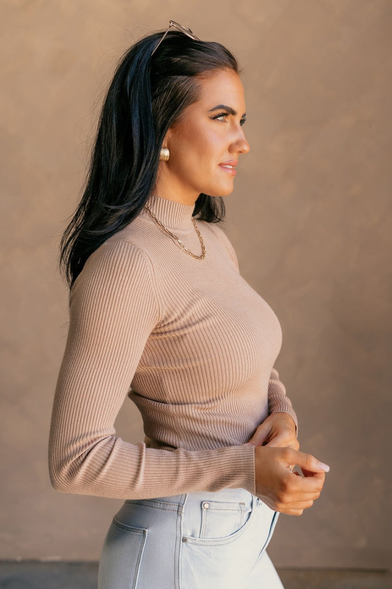 Side view of model wearing the Mila Khaki Ribbed Long Sleeve Top which features khaki ribbed knit fabric, a high neckline, and long sleeves.