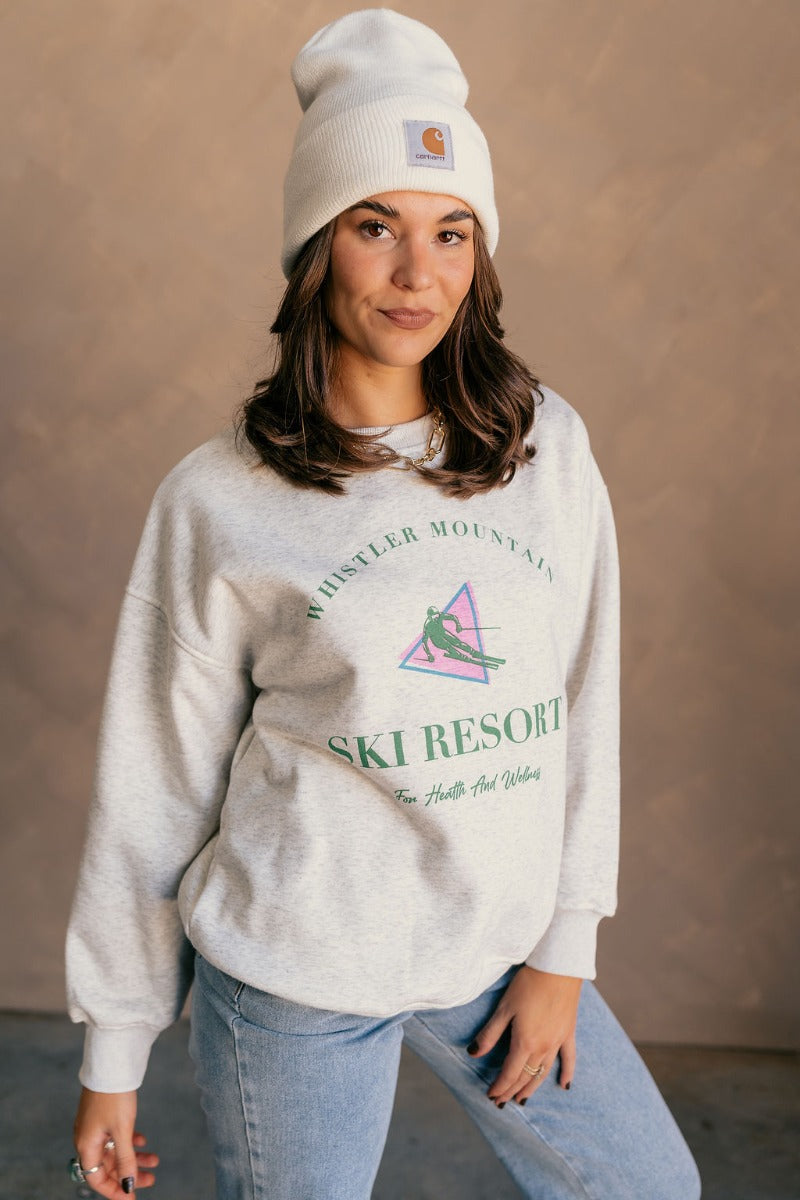 Front view of model wearing the Whistler Mountain Ski Resort Heather Grey Sweatshirt which features heather grey knit fabric, round neckline, ribbed hem and long sleeves with cuffs. Graphic says "Whistler Mountain Ski Resort" in green "For Health and Well