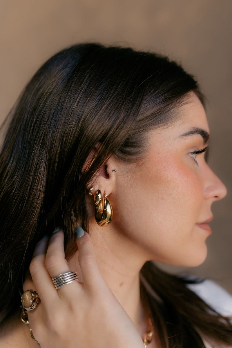 Side view of model wearing the Elodie Gold Scoop Hoop which features small gold scooped, open hoops.