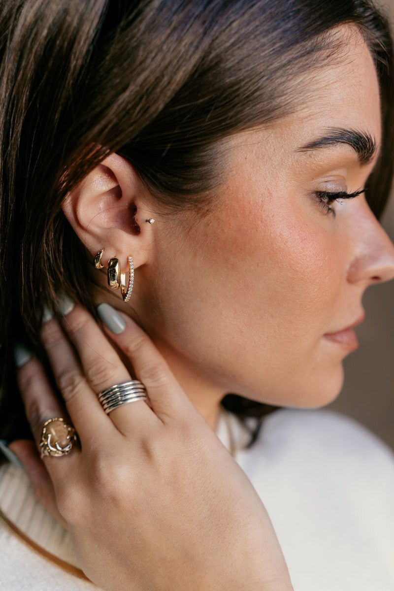 Side view of model wearing the Esme Gold Rhinestone Teardrop Hoop which features gold tear drop-shaped huggies with clear stones.