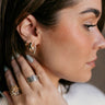 Side view of model wearing the Esme Gold Rhinestone Teardrop Hoop which features gold tear drop-shaped huggies with clear stones.